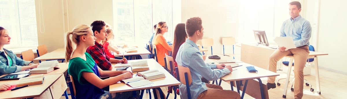 Un grupo de estudiantes escucha atentamente a un profesor en un aula iluminada.