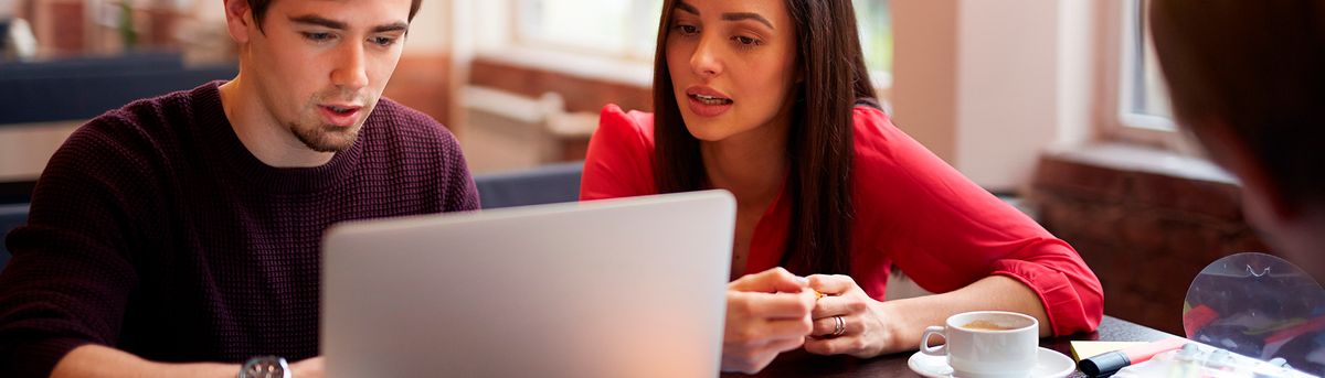 Una pareja de jóvenes revisa algo en una computadora portátil en un café.