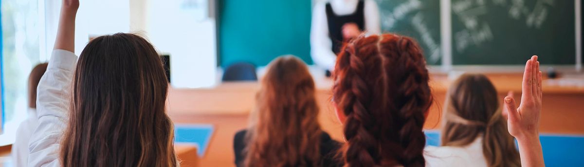 Un grupo de estudiantes en un aula levantando la mano para participar.