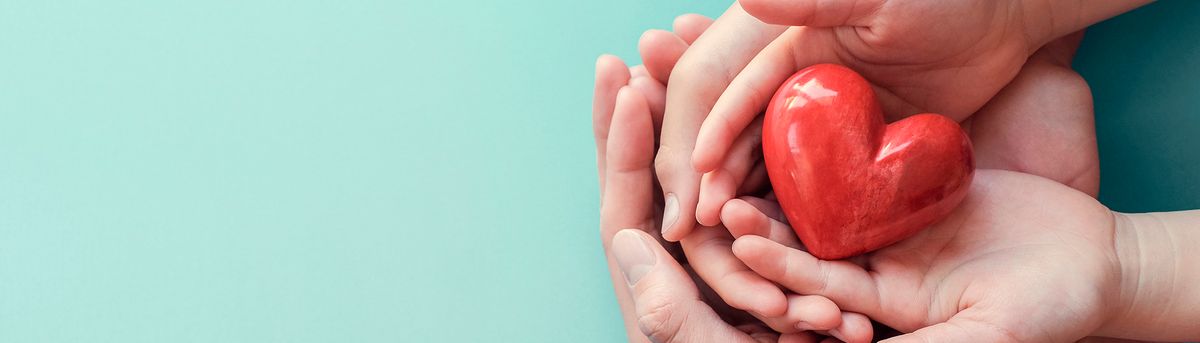 Varias manos sostienen un corazón rojo sobre un fondo azul claro.