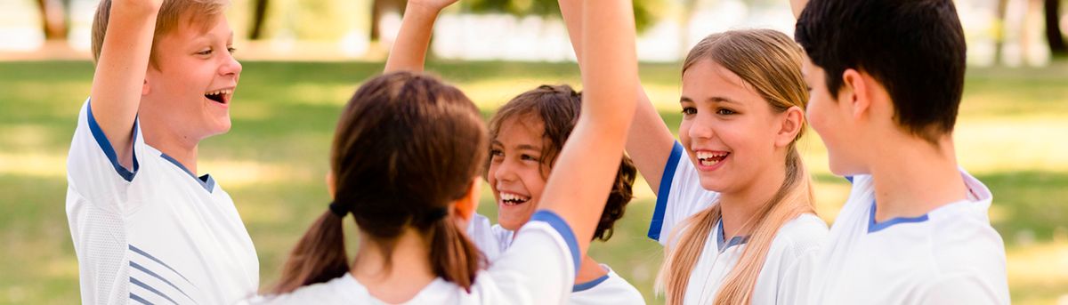 Un grupo de niños sonrientes celebrando con los brazos en alto en un ambiente al aire libre.
