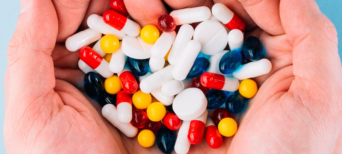 Unas manos sosteniendo una variedad de pastillas y cápsulas de colores.