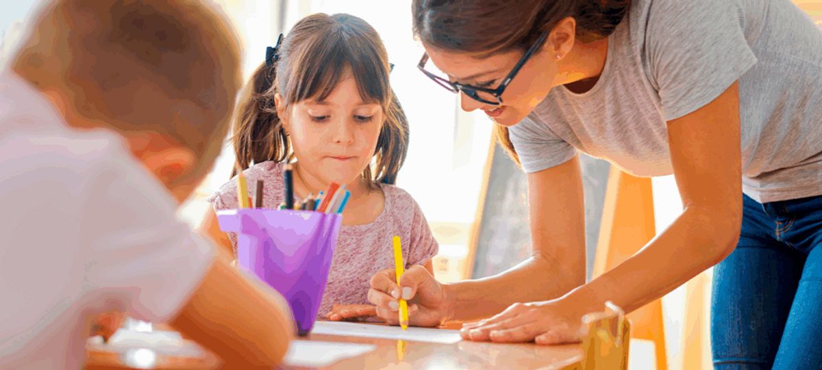Una profesora ayuda a una niña a dibujar en una mesa llena de materiales de arte.