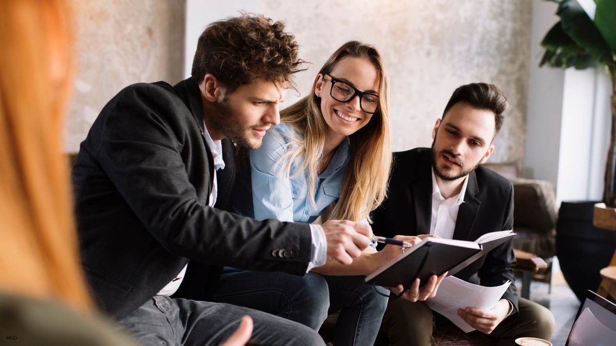 Un grupo de tres personas se encuentra en una reunión colaborativa, revisando notas y compartiendo ideas.