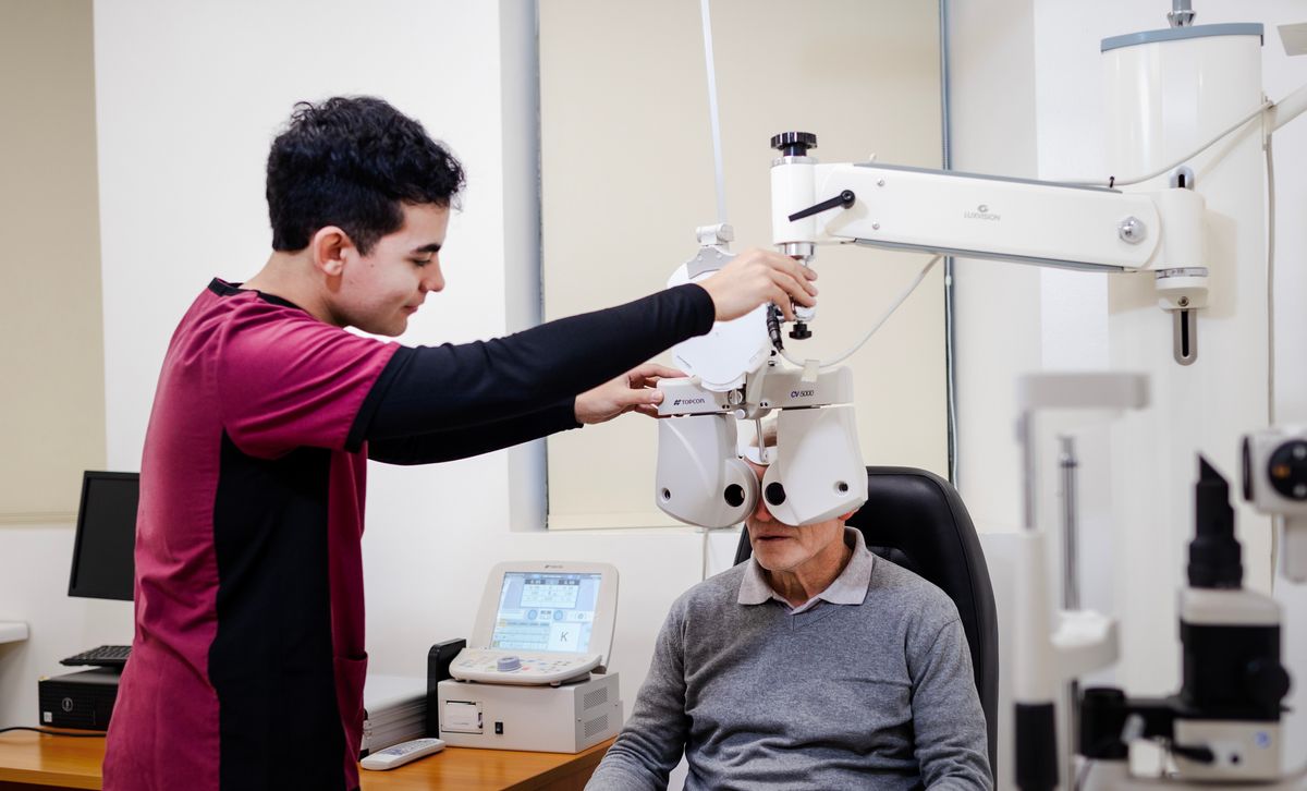 Un joven está ayudando a un adulto mayor en un examen de vista en una clínica.