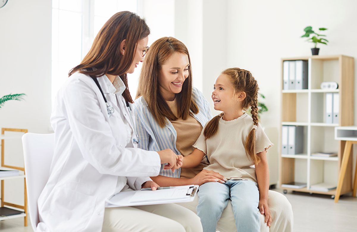 Una doctora sonriente atiende a una mamá y su hija en una consulta médica.