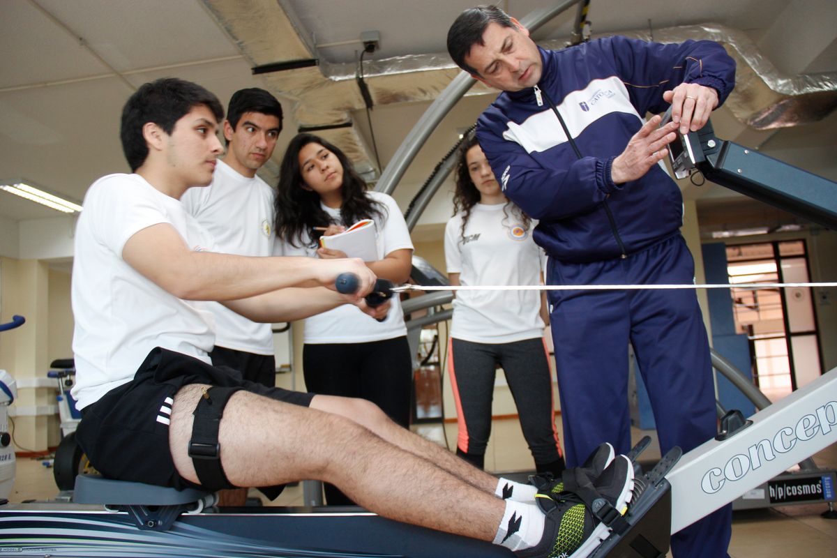 Un grupo de jóvenes está aprendiendo sobre el uso de una máquina de remo en un gimnasio.