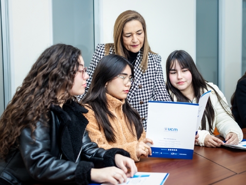 Un grupo de estudiantes está revisando documentos con una profesora en una sala de clases.