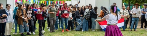 Un grupo de personas observa a una bailarina que se presenta con una bandera en un evento al aire libre.