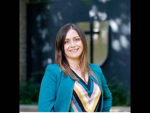 Una mujer sonriente con chaqueta azul y fondo difuso en una institución.