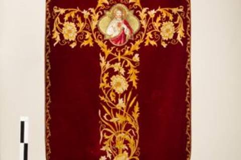 Una cruz decorada con bordados dorados sobre un fondo rojo, con una imagen en el centro.