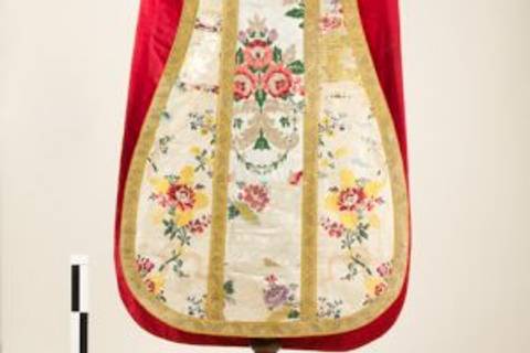 Es un delantal decorado con bordados florales en tonos pastel y un fondo blanco, con un borde rojo.