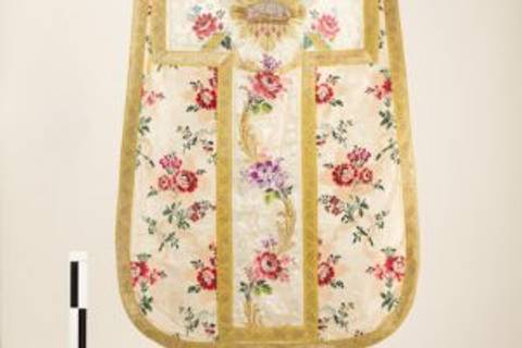 La imagen muestra un paramento decorado con flores en tonos rosados y dorados.