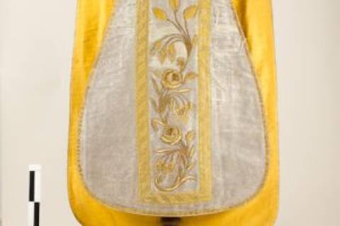 Un delantal bordado con tonos amarillos y plateados que muestra un diseño floral.
