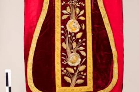 La imagen muestra un tapiz de color rojo con bordados dorados y detalles florales en el centro.