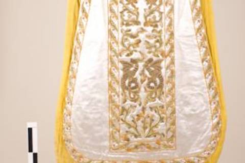 La imagen muestra una prenda decorada con bordados dorados sobre un fondo blanco y amarillo.