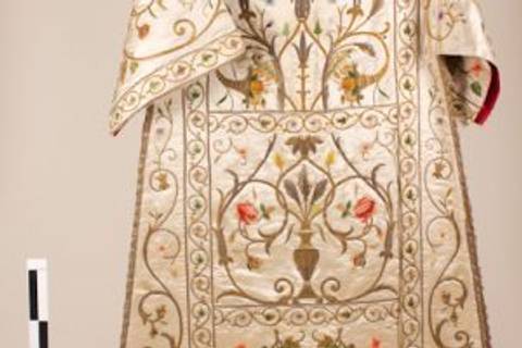 La imagen muestra una vestimenta ceremonial rica en detalles y bordados florales.