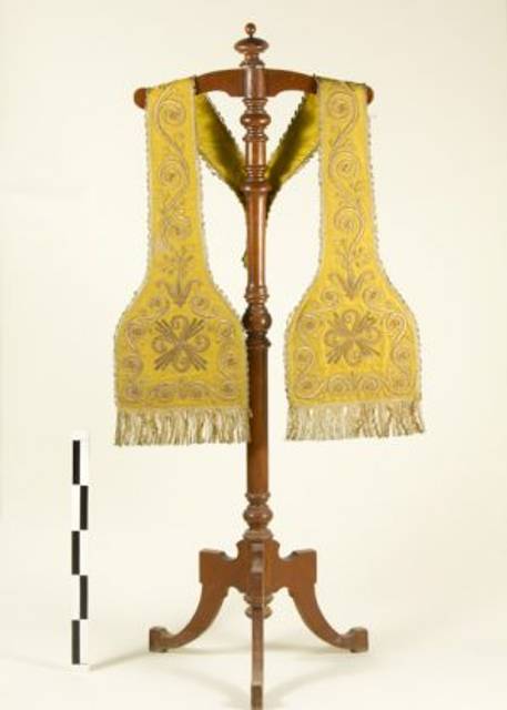 Un chal amarillento con bordados decorativos está colgado en un perchero de madera.