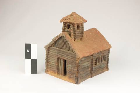 La imagen muestra una maqueta de una cabaña de madera con un techo de palapa.