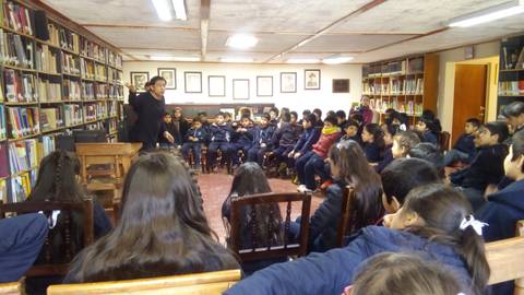 Un grupo de niños escucha atento a un maestro en una biblioteca.