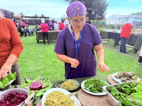 Una mujer en un evento al aire libre prepara ensaladas con ingredientes frescos.