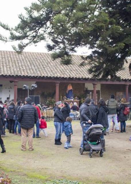 Un grupo de personas congregadas en un evento al aire libre frente a un edificio con una techumbre de tejas.