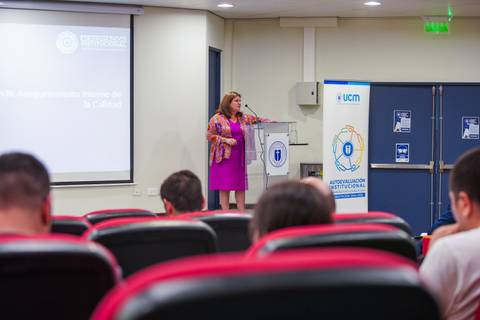 Una mujer presenta en una conferencia en un auditorio con público atento.