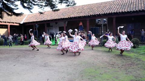 Un grupo de mujeres baila en un evento tradicional vistiendo faldas con flores.