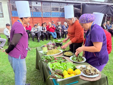 Un grupo de mujeres presenta una demostración culinaria al aire libre para una audiencia de adultos mayores.