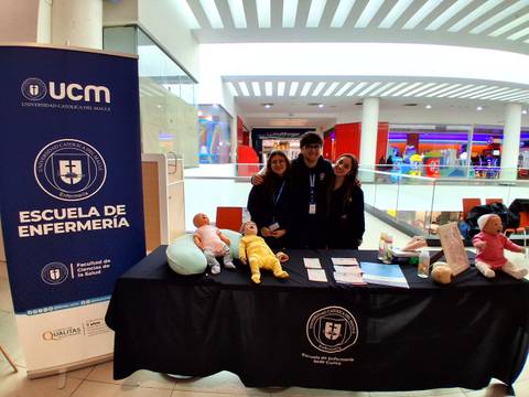 Un grupo de estudiantes de enfermería posando en un stand de la universidad con maniquíes de bebés.