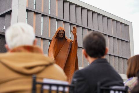 Una escultura impactante de una figura con túnica que llama la atención frente a un edificio moderno.