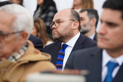 Un grupo de personas atenta a un evento al aire libre, con un hombre de gafas al frente mostrando interés.