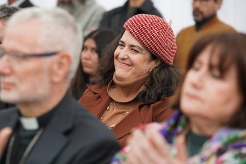 Una mujer sonriente con un gorro rojo se destaca entre una audiencia seria en un evento.