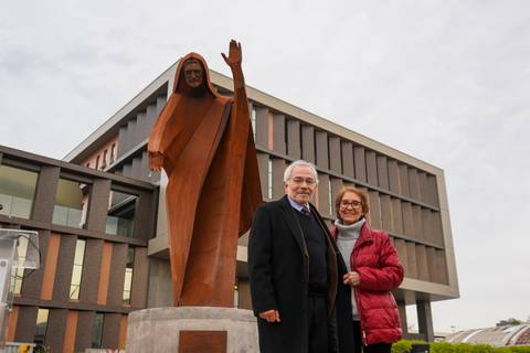 Un par de personas sonríen frente a una escultura impresionante en un día nublado.