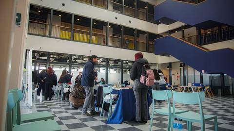 Un grupo de personas interactuando dentro de un espacio amplio y moderno, con mesas y sillas, en un ambiente de trabajo o evento.