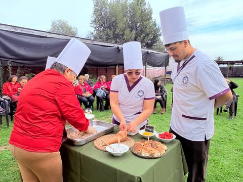 Un grupo de personas preparan comida en un evento al aire libre, mientras un público observa atentamente.