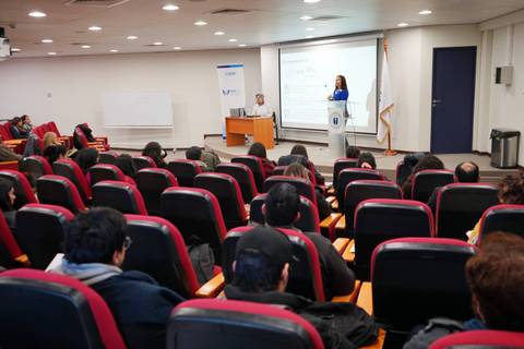 Una charla en un auditorio, con una persona exponiendo frente a un público atento.