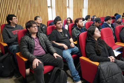Un grupo de estudiantes sentados en asientos rojos en un lugar de clases.