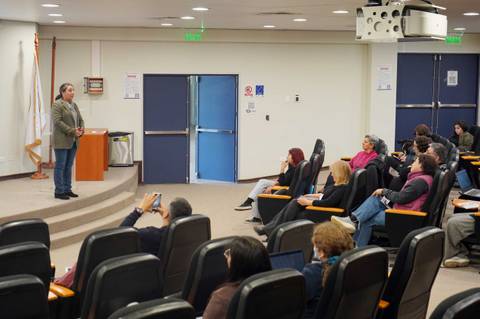 Una charla en un auditorio con un expositor frente a un grupo de personas sentadas.