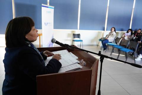 Una mujer habla en un podio mientras un grupo la escucha atentamente.