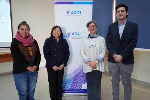 Cuatro personas posando junto a un banner de la UCM durante un evento académico.
