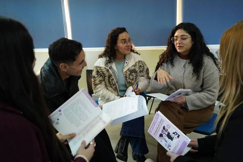 Un grupo de jóvenes conversando y compartiendo documentos en un ambiente de aprendizaje.