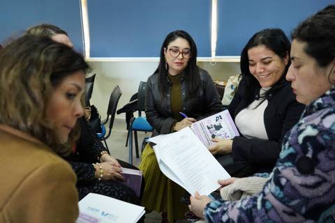 Un grupo de mujeres en una reunión, conversando sobre documentos y tomando notas.