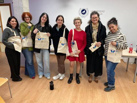 Un grupo de mujeres posando sonrientes con bolsas de tela en una sala de universidad.