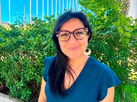 Mujer sonriente posando frente a un fondo verde en un día soleado.
