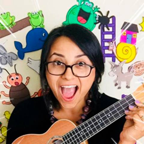 Una persona sonriente sostiene una guitarra pequeña mientras está rodeada de coloridos dibujos en la pared.
