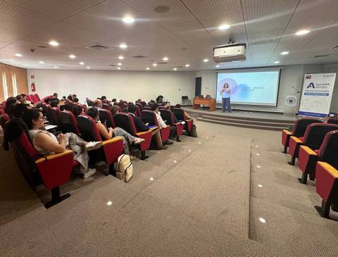 Una conferencia en un auditorio con varias personas escuchando a la presentadora.