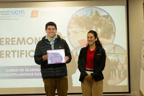 Un joven sonriente sostiene un certificado durante una ceremonia de entrega en un curso de reanimación cardiopulmonar.
