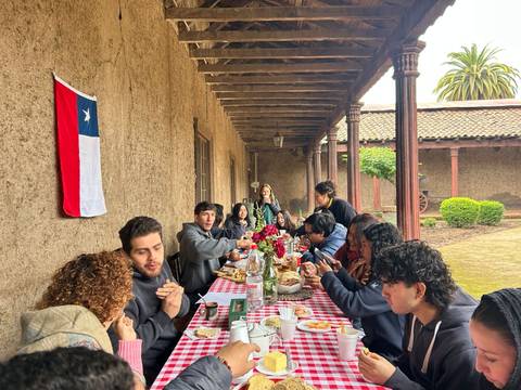 Una grupo de amigos compartiendo un almuerzo en un día nublado con una bandera chilena de fondo.