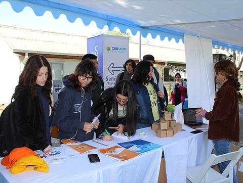Un grupo de estudiantes interactúa en un stand informativo, recolectando material y firmando en una actividad educativa.